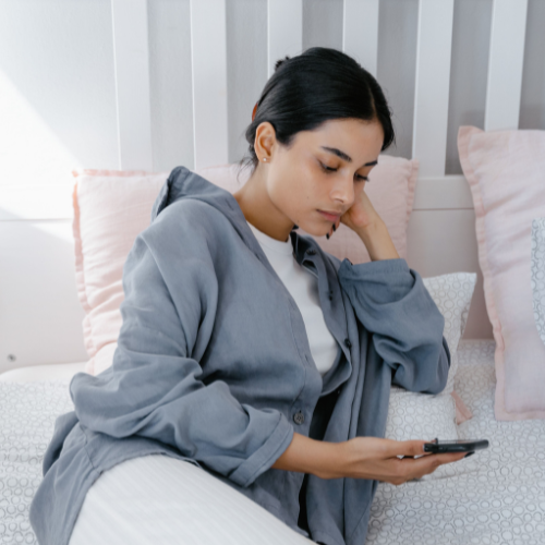 Young woman sitting on her bed and looking at her phone after a breakup