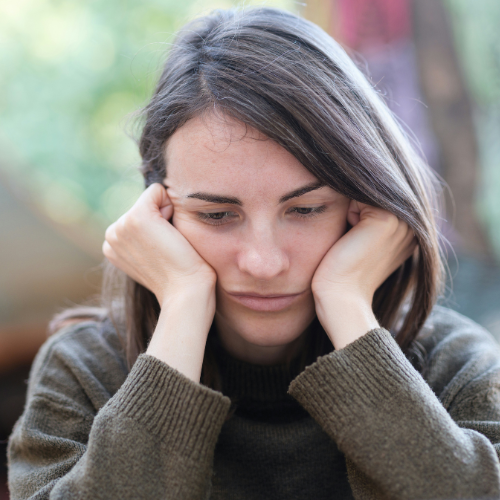 Young woman sitting with her hands against her face while feeling anxious